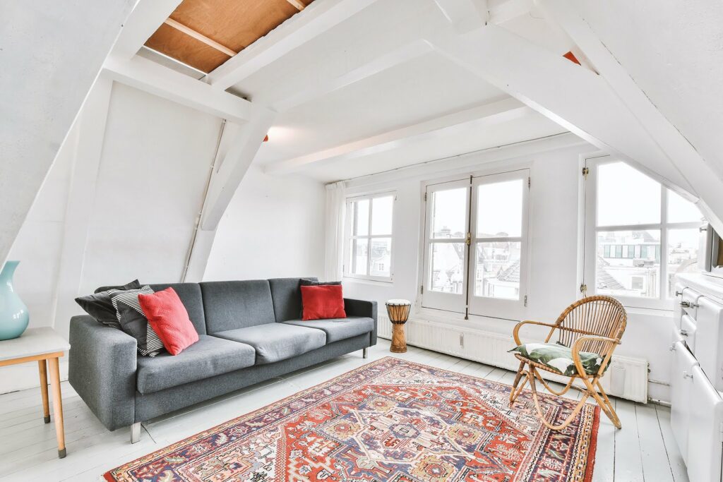 bright attic living room with grey sofa patterned area rug large windows white beams and cozy seating arrangement