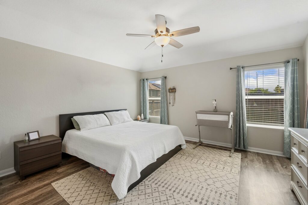 light hardwood flooring in bright bedroom with neutral area rug large windows and minimalist decor