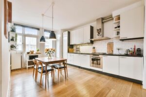 light hardwood flooring in contemporary kitchen and dining area with white cabinetry and modern finishes